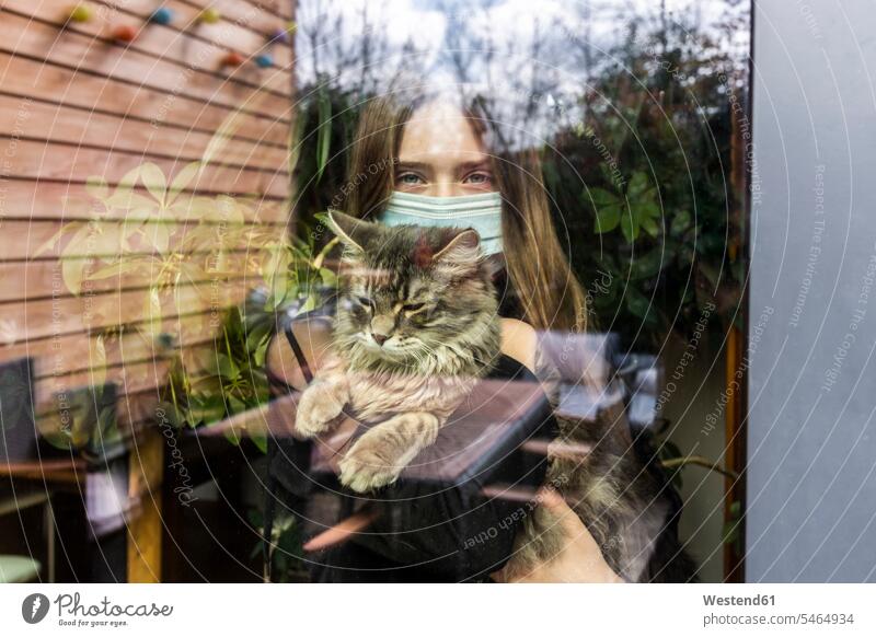 Portrait of girl with surgical mask and cat behind window pane animals creature creatures domestic animal pet cats windows panes window glass window glasses