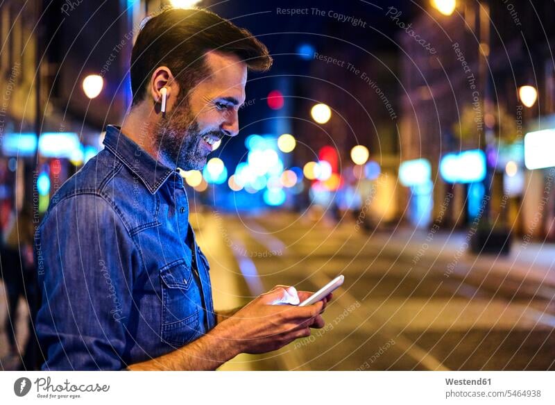 Man with wireless headphones using smartphone in the city at night human human being human beings humans person persons caucasian appearance caucasian ethnicity