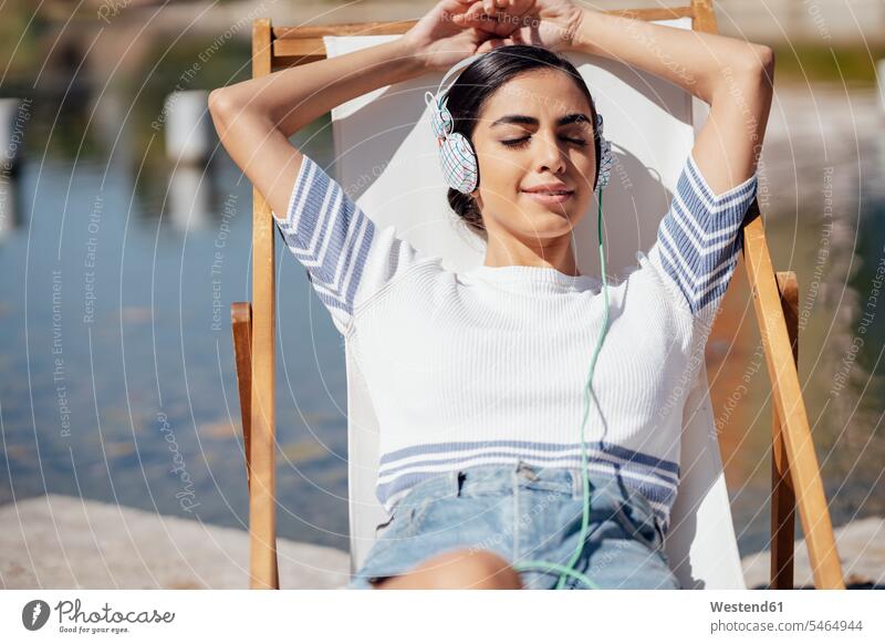 Young woman wearing headphones relaxing in a deckchair T- Shirt t-shirts tee-shirt chairs deck chair deck chairs deckchairs headset hear smile Seated sit