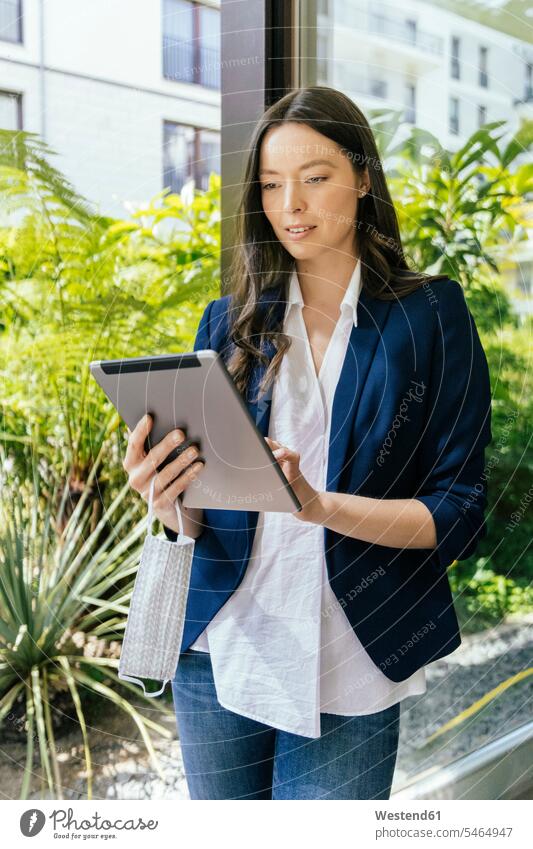 Businesswoman with face mask in hand using tablet at glass pane Occupation Work job jobs profession professional occupation business life business world