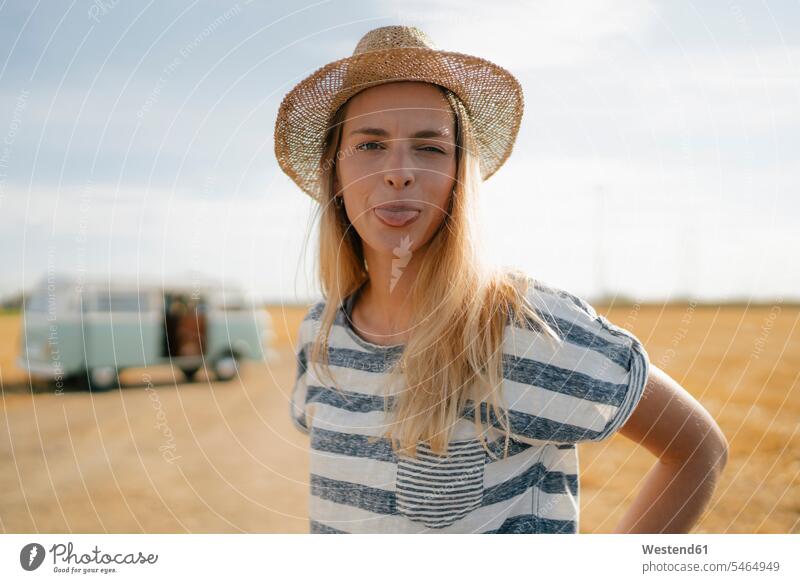 Portrait of young woman at camper van in rural landscape sticking out her tongue females women landscapes scenery terrain Camper portrait portraits country