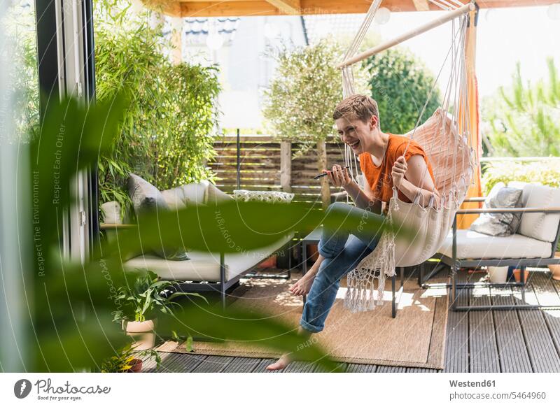 Cheerful woman talking over mobile phone while swinging in porch seen through indoors color image colour image Germany leisure activity leisure activities