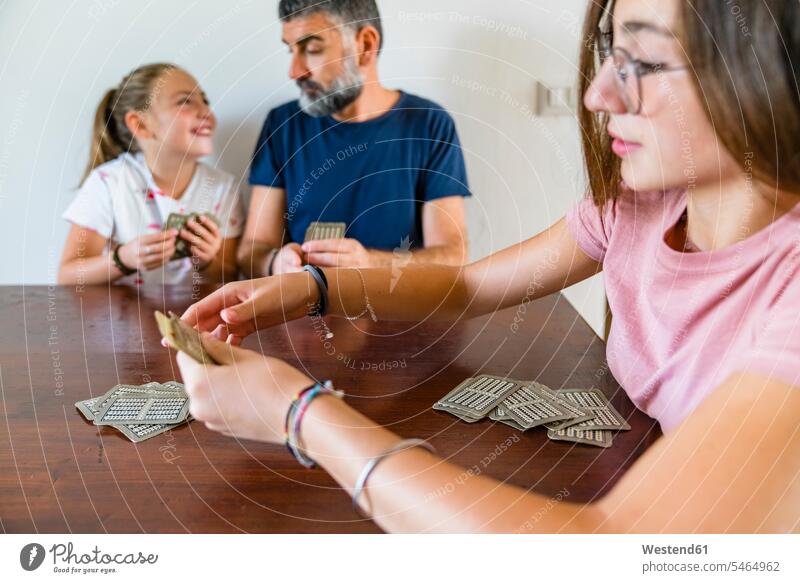 Father with two daughters playing cards on wooden table at home T- Shirt t-shirts tee-shirt Tables wood table games parlor games parlour game parlour games