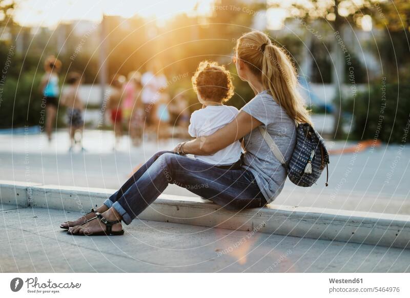 Mther sitting with her little son on a square at sunset plaza places Public Square sunsets sundown mother mommy mothers ma mummy mama Seated sons manchild