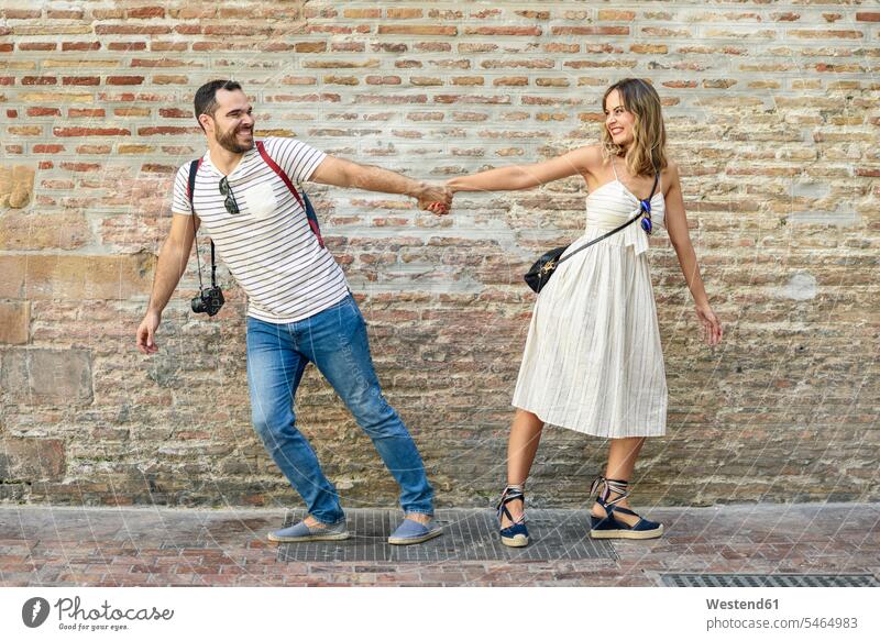 Happy couple holding hands walking in opposite directions at brick wall twosomes partnership couples happiness happy brick walls going people persons
