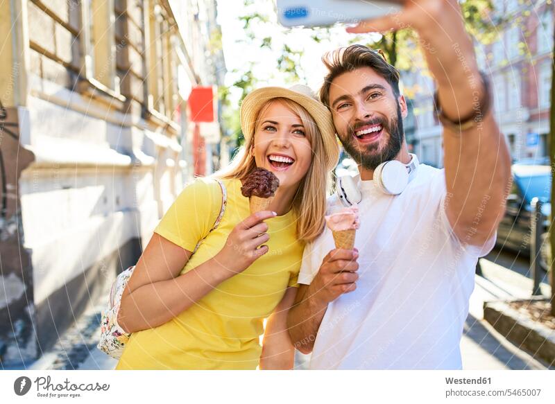 Happy young couple taking a selfie while eating ice cream in the city touristic tourists hats T- Shirt t-shirts tee-shirt headphone headset telecommunication
