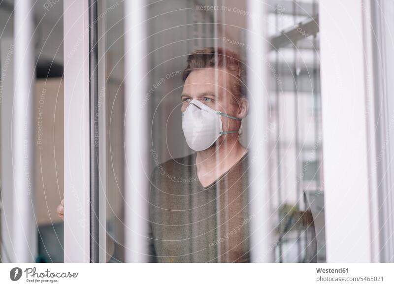 Portrait of man wearing protective mask behind at the window windows pane panes window glass window glasses Window Pane windowpanes glass panes contemplative