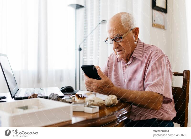 Senior man using smart phone while doing research on mineral and fossil at home color image colour image indoors indoor shot indoor shots interior interior view