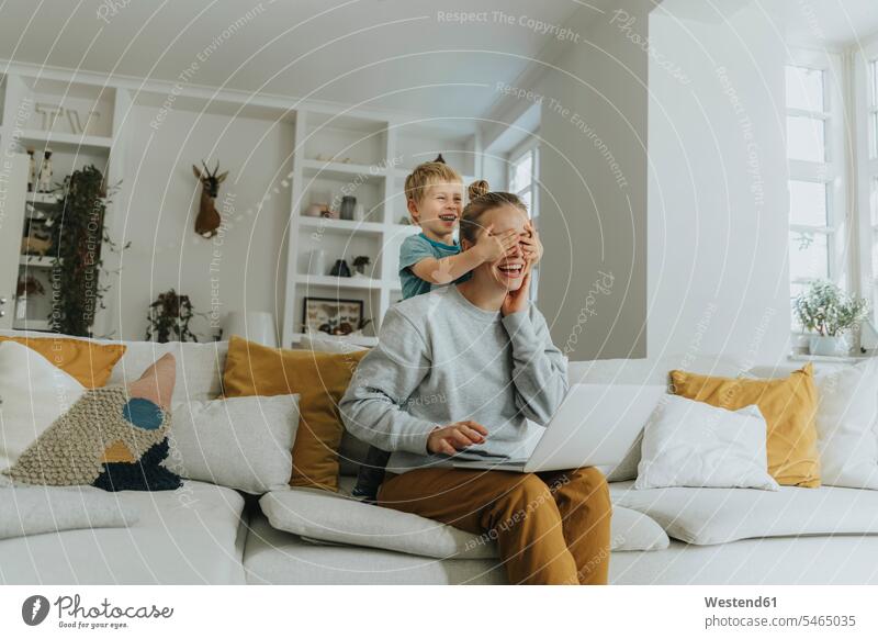 Smiling boy covering mother eyes while standing on sofa at home color image colour image indoors indoor shot indoor shots interior interior view Interiors day