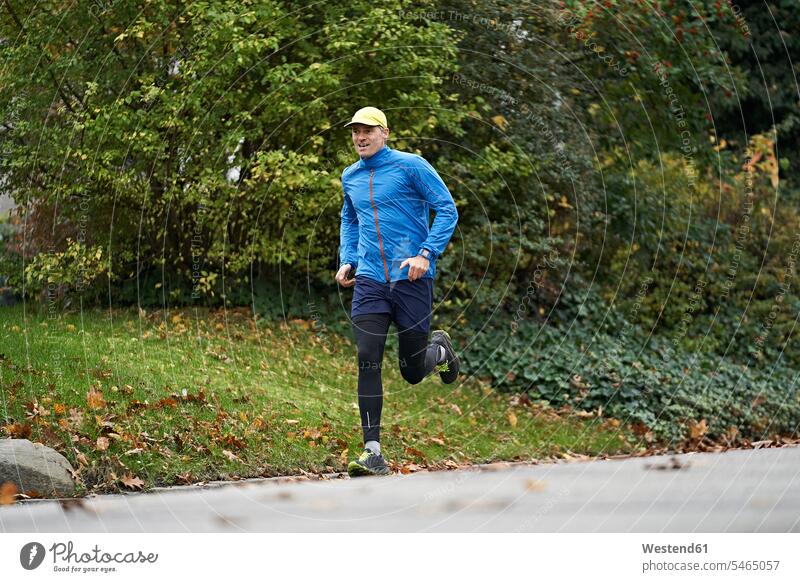 Mature man in sports clothing running on footpath by grass color image colour image outdoors location shots outdoor shot outdoor shots day daylight shot