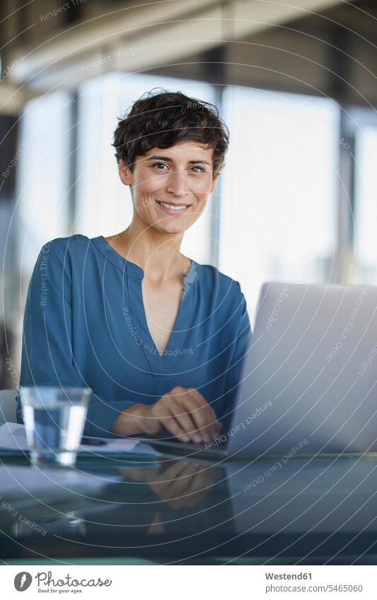 Portrait of confident businesswoman sitting at desk in office with laptop businesswomen business woman business women offices office room office rooms portrait