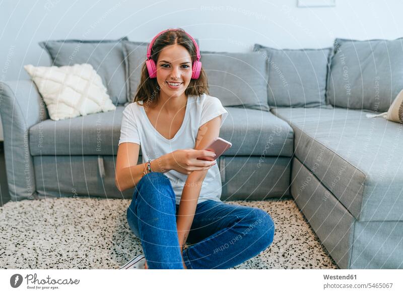 Portrait of smiling young woman sitting on floor in living room listening to music with cell phone human human being human beings humans person persons