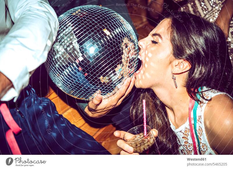 Young woman with eyes closed holding drink and biting disco ball in glamorous party color image colour image indoors indoor shot indoor shots interior