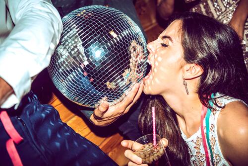 Young woman with eyes closed holding drink and biting disco ball in glamorous party color image colour image indoors indoor shot indoor shots interior