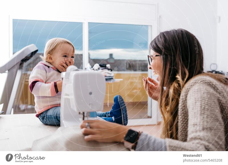 Happy mother with little daughter at home using sewing machine happiness happy sewing machines mommy mothers mummy mama daughters device devices parents family