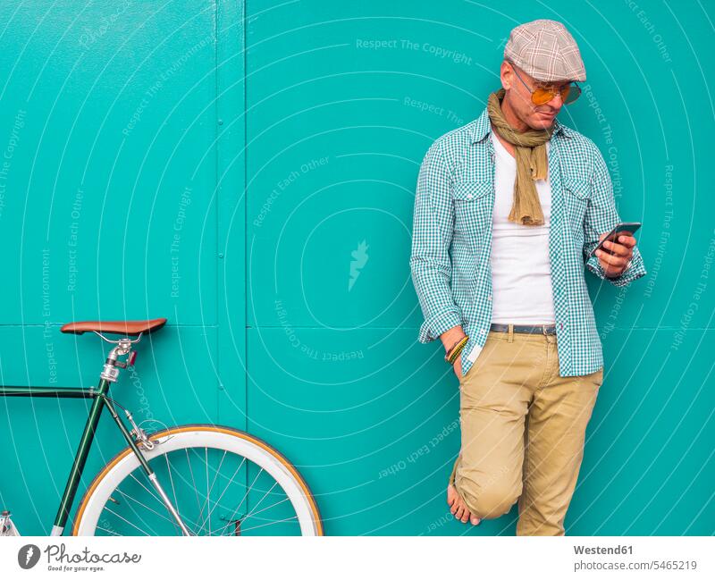 Man with Fixie bike standing in front of green wall looking at cell phone scarfs scarves bikes cycle cycles bicycles telecommunication phones telephone
