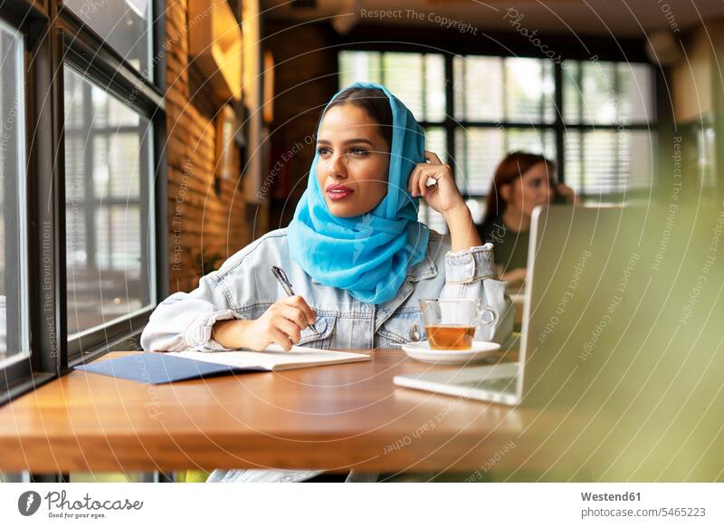 Businesswoman wearing turquoise hijab in a cafe and writing in notebook human human being human beings humans person persons caucasian appearance