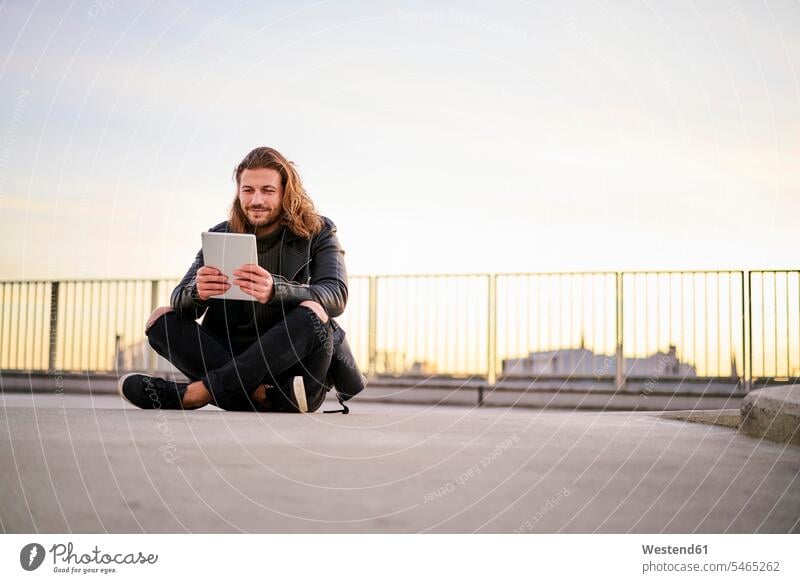 Portrait of bearded young man sitting on parking level at twilight using digital tablet digitizer Tablet Computer Tablet PC Tablet Computers iPad Digital Tablet