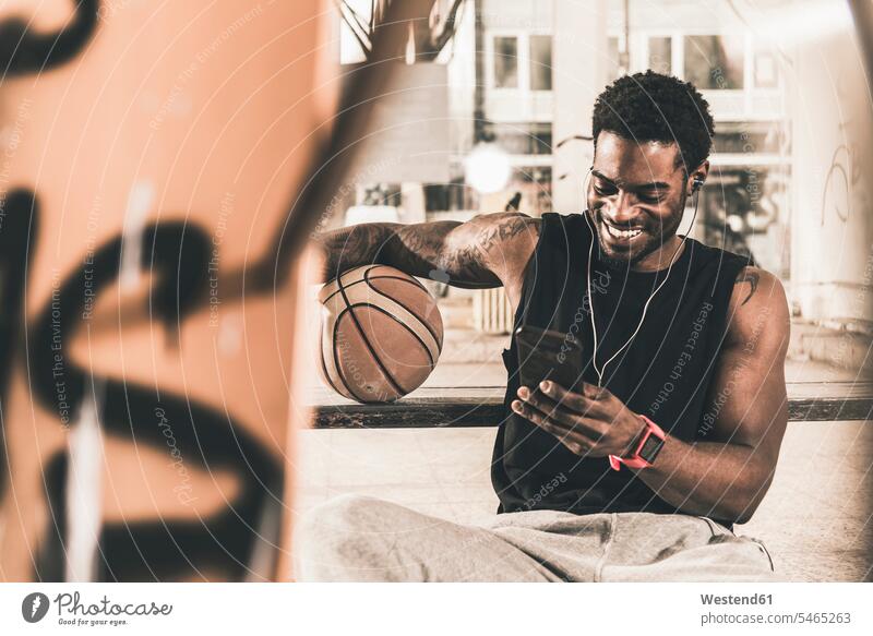Smiling man with tattoos and basketball using smartphone and earphones men males smiling smile ear phone ear phones basketballs Smartphone iPhone Smartphones