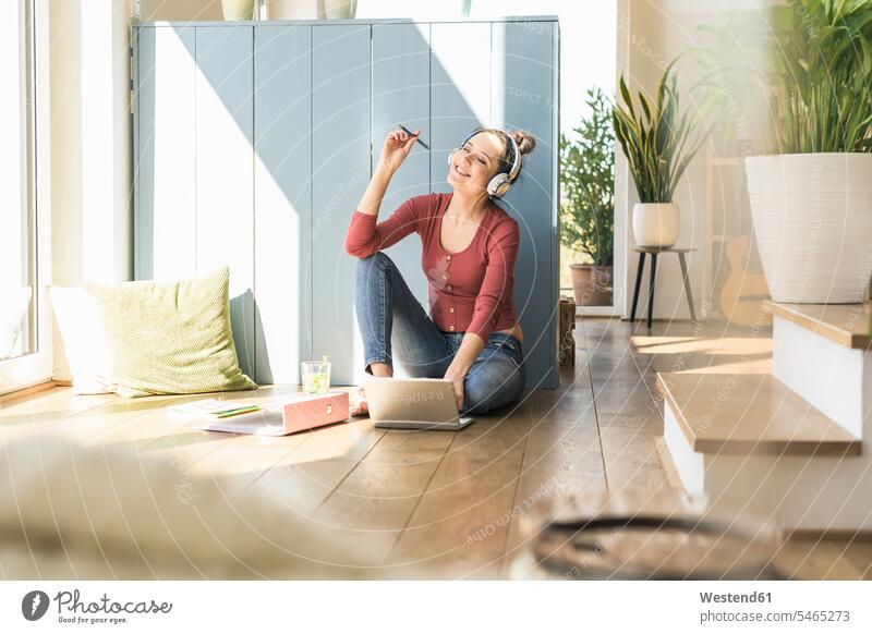 Woman with headphones sitting at the window at home using laptop woman females women Seated headset windows Laptop Computers laptops notebook Adults grown-ups