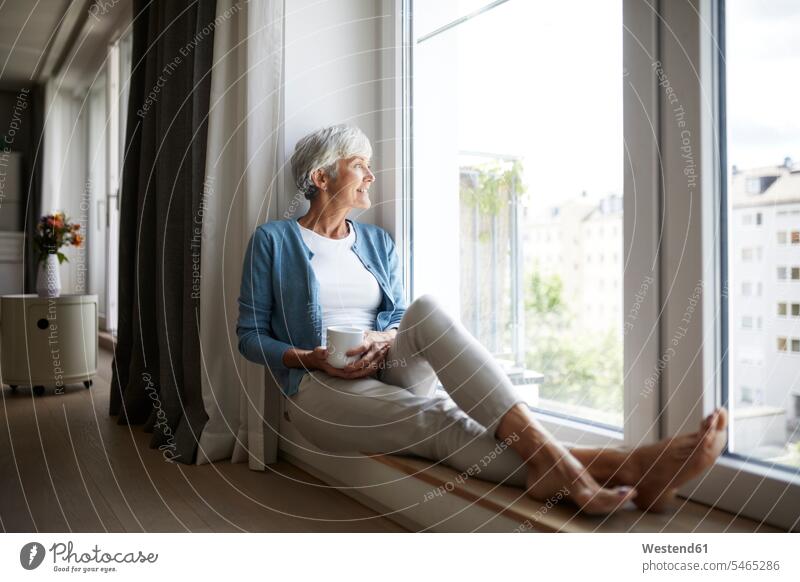 Smiling senior woman looking through window while sitting at home color image colour image indoors indoor shot indoor shots interior interior view Interiors day