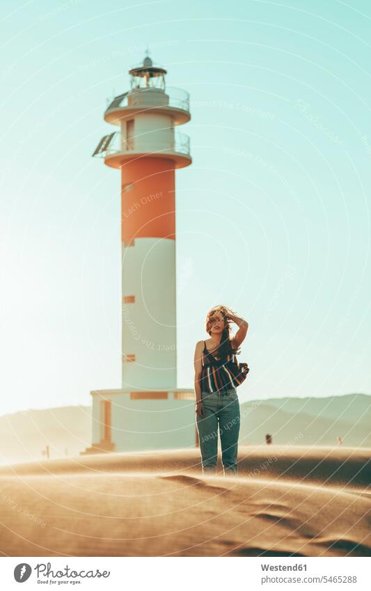Young woman with windswept hair standing in desert landscape at lighthouse landscapes scenery terrain females women lighthouses light houses blowing Deserts