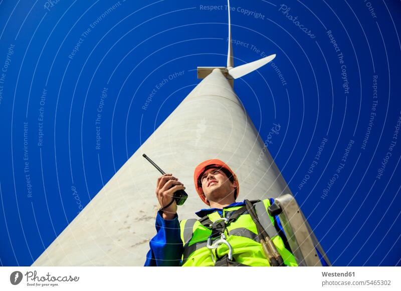 Low angle view of technician with walkie-talkie in front of wind turbine walkie talkie walkie-talkies walkie talkies two-way radios wind turbines technicians
