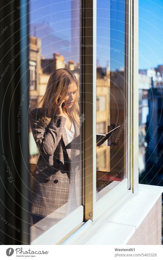 Young businesswoman standing at the window, talking on the phone office offices office room office rooms call telephoning On The Telephone calling working