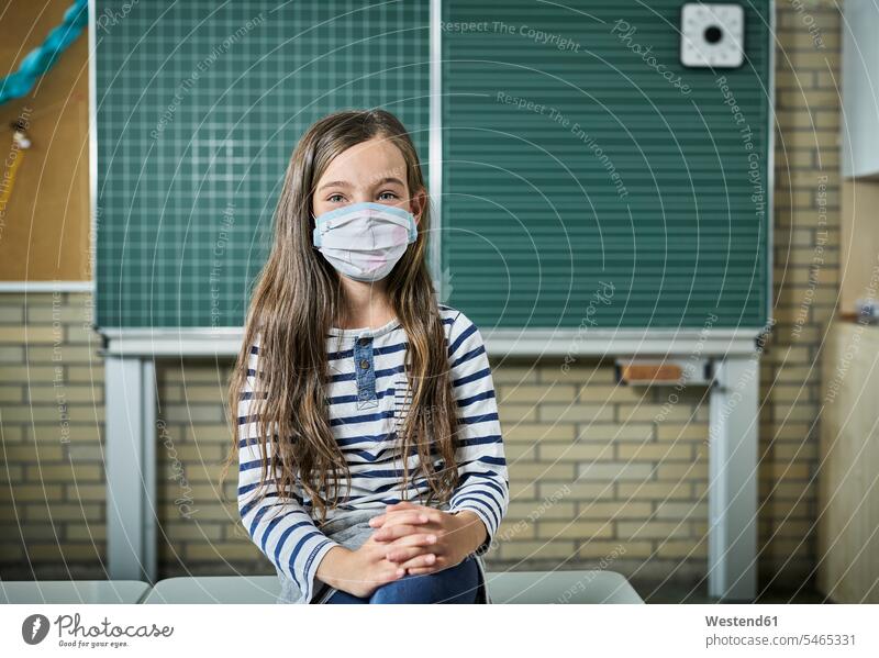 Portrait of girl wearing mask in classroom pupils schoolchild schoolchildren blackboards smile Seated sit healthy protect protecting safe Safety secure