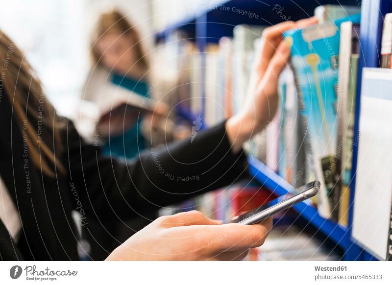 Hand of teenage girl holding cell phone while taking book from shelf in a public library books Smartphone iPhone Smartphones hand human hand hands human hands