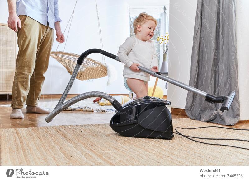 Cute baby boy holding vacuum cleaner while standing on carpet by father at home color image colour image Germany indoors indoor shot indoor shots interior