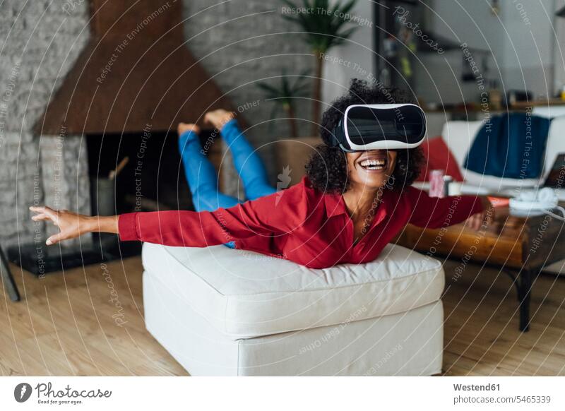 Woman lying on seating furniture, wearing VR goggles, pretending to fly Pretending To Fly Pretending to be a plane mid adult women mid adult woman