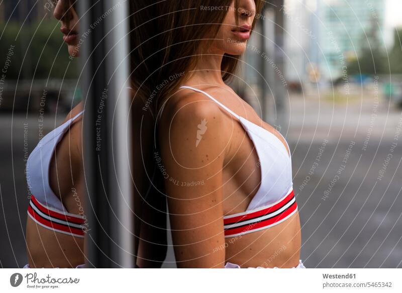 Close-up of attractive young woman in sportswear leaning against glass front of a building Sportswear Activewear Sport Clothes Sports Clothes Sports Wear