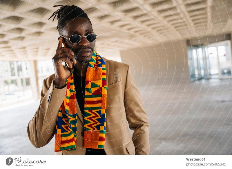 Fashionable man wearing traditional kenete talking on phone while standing in building color image colour image indoors indoor shot indoor shots interior