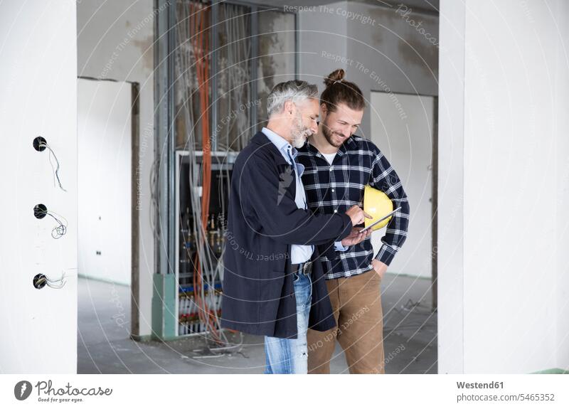 Architect and construction worker discussing over digital tablet while standing in renovating house color image colour image Germany Architecture