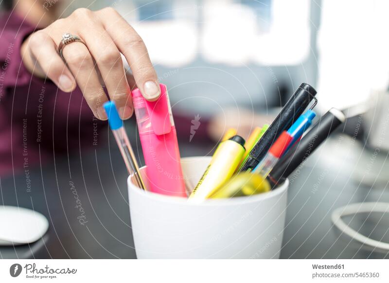 Woman at desk in office taking highlighter from penholder woman females women highlighters marker pen offices office room office rooms desks businesswoman