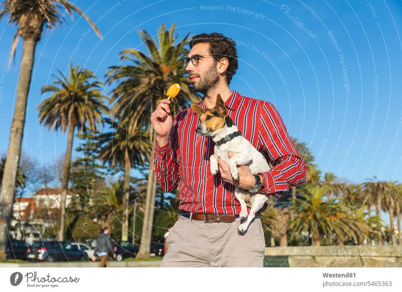 Young man with dog on his arm eating ice lolly single singles celibate solitary people celibates solitary person Palm Palm Trees Palms one animal 1 copy space