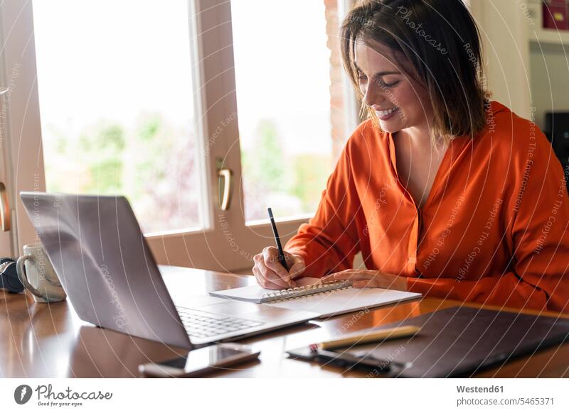 Smiling businesswoman writing in notepad while working at home color image colour image indoors indoor shot indoor shots interior interior view Interiors day