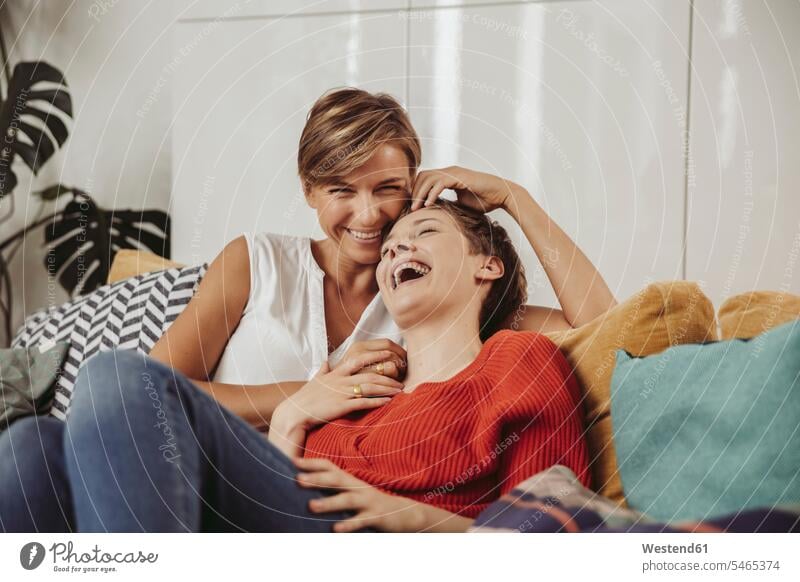 Happy lesbian couple laughing and cuddling on couch happiness happy twosomes partnership couples snuggle cuddle snuggling settee sofa sofas couches settees