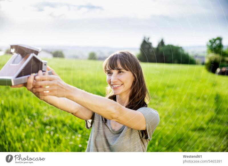 Smiling brunette woman taking instant photo on a meadow human human being human beings humans person persons caucasian appearance caucasian ethnicity european 1