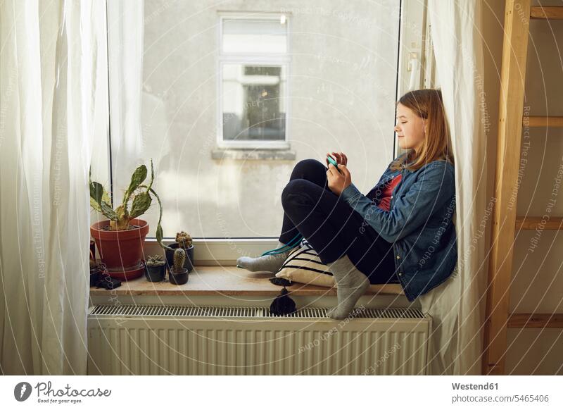 Girl sitting at the window at home using smartphone flower pot flower pots flowerpots windows telecommunication phones telephone telephones cell phone