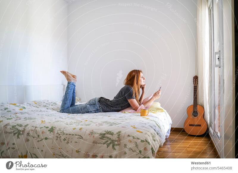Young woman at home chilling in bedroom and using her smartphone human human being human beings humans person persons caucasian appearance caucasian ethnicity