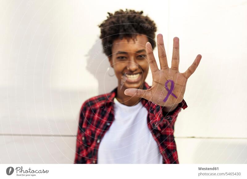 Happy young woman showing purple awareness symbol on palm against white wall during Womens Day color image colour image Spain outdoors location shots