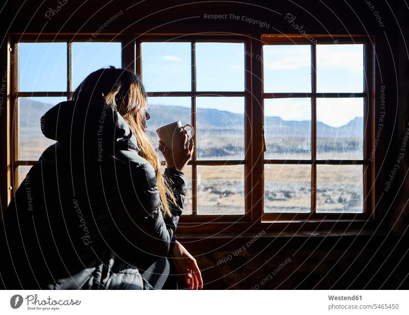 Woman having a cup of coffee while admiring the mountains through the window touristic tourists windows pane panes window glass window glasses Window Pane