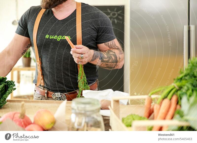 Vegan man holding carrot in his kitchen mature men mature man Carrot Carrots Vegetable Vegetables vegan cooking vegetarian veggie veggy vegetarians