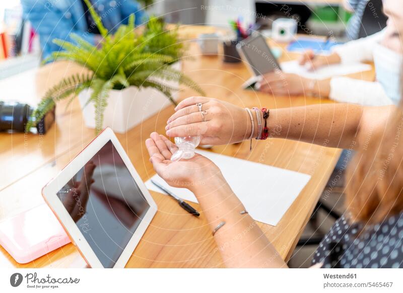 Mid adult woman using hand sanitizer while working with coworker at office color image colour image indoors indoor shot indoor shots interior interior view