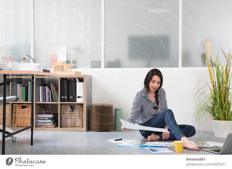 Casual woman with plans and laptop sitting on the floor in a loft office casual Laptop Computers laptops notebook females women floors lofts offices office room
