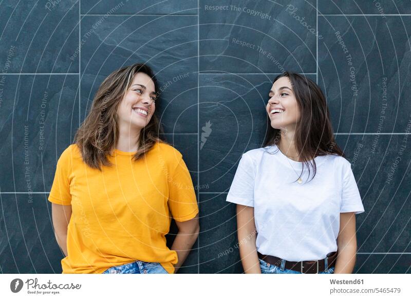 Two friends leaning on a gray wall and laughing human human being human beings humans person persons caucasian appearance caucasian ethnicity european
