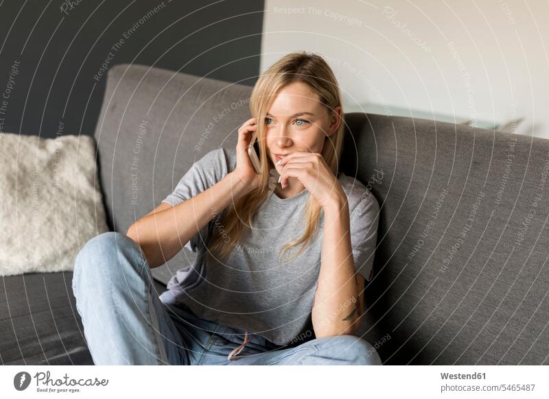 Smiling young woman sitting on couch talking on cell phone females women smiling smile on the phone call telephoning On The Telephone calling Seated