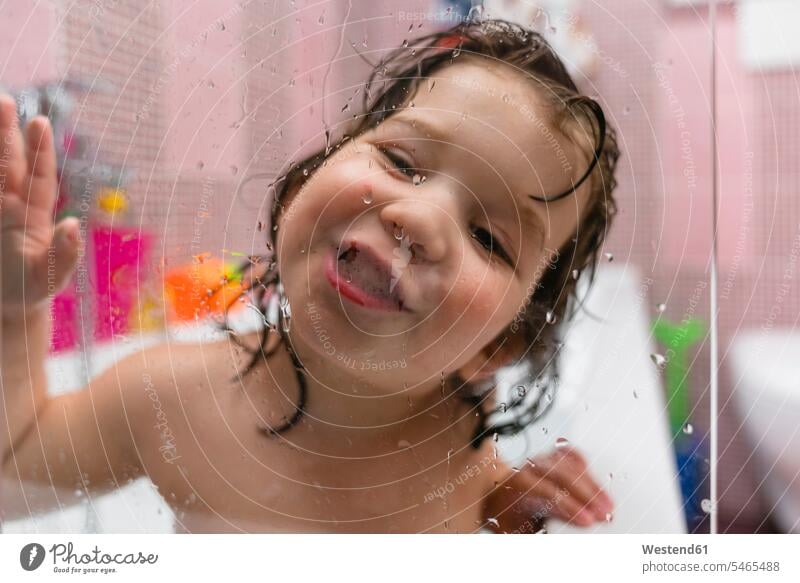 Portrait of happy little girl in bathtub behind glass pane bath tub bath tubs bathtubs windows glass panes bathe Taking A Bath smile play relax relaxing